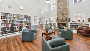 Interior Victoria Park at Edgewater, clubhouse, various bookshelves, large stone fireplace, various lounge chairs, wood floors, computer room in back of room.