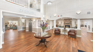 Interior Victoria Park at Edgewater lobby, Avanath signage on second story catwalk, fireplace in lobby, rustic decor, entrance table, wood floors, white walls.