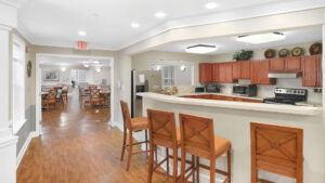 Interior Victoria Park at Edgewater community kitchen, barstool seating attached to countertop. wood cabinetry, stainless steel appliances, wood floors, white walls.